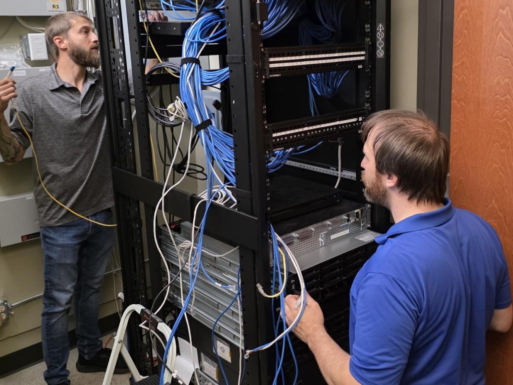 Two CCB Technology technicians working on a network rack in a client server room